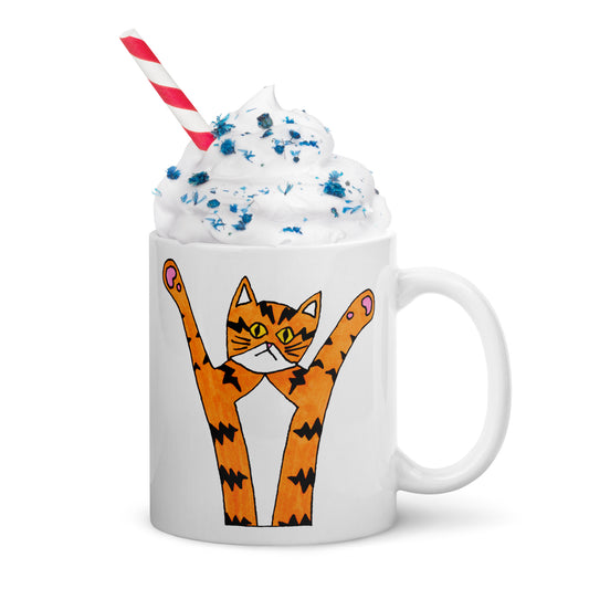 A white mug with a drawing of an orange cat with tiger stripes and his paws in the air. Whipped cream and a red and white straw are in it.